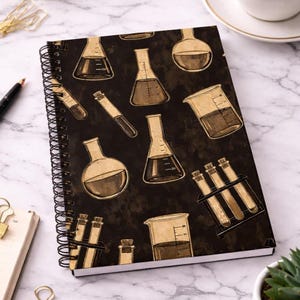 Puede incluir: Un cuaderno de espiral con una cubierta marrón oscuro que presenta un patrón repetido de cristalería científica en tonos marrones y beige. Las páginas del cuaderno son visibles y la encuadernación en espiral es negra.