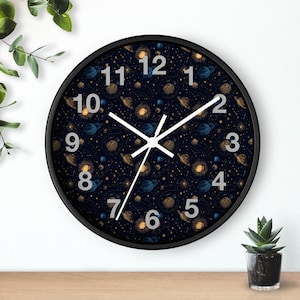 Puede incluir: Un reloj de pared redondo negro con un fondo azul oscuro adornado con un patrón de planetas y estrellas. La esfera del reloj muestra números y manecillas blancas. El diámetro del reloj es de aproximadamente 30 cm.