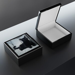 May include: A black wooden box with a hinged lid. The box is open and the inside is lined with white felt. The box has a photo of a black cat on the top.
