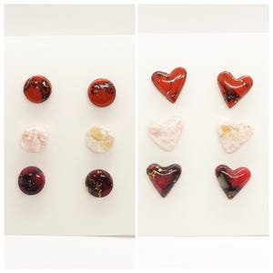 May include: Set of six resin earrings in various shapes and colors. The set includes two red round earrings, two red heart earrings, and two white heart earrings. Each earring has a unique marbled pattern.