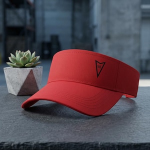 May include: A bright red visor featuring a black triangular logo with the number 65 printed inside. The visor has a curved brim with visible stitching and an open top design, constructed from a solid fabric material with a structured front panel.