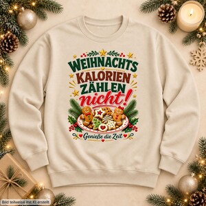 May include: A beige crewneck sweatshirt featuring a graphic print with the German text "WEIHNACHTS KALORIEN ZÄHLEN nicht!" and "Genieße die Zeit". The design includes illustrations of gingerbread cookies, pine branches, and stars.