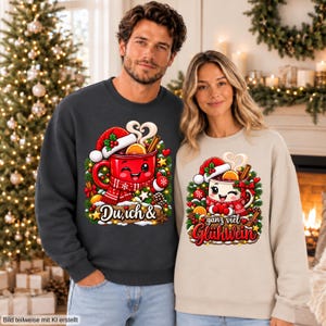 May include: A dark charcoal gray sweatshirt and a beige sweatshirt, each featuring a graphic of a smiling red mug wearing a Santa hat and scarf, surrounded by pine branches and ornaments, with the text Du, ich & ganz viel Glühwein.