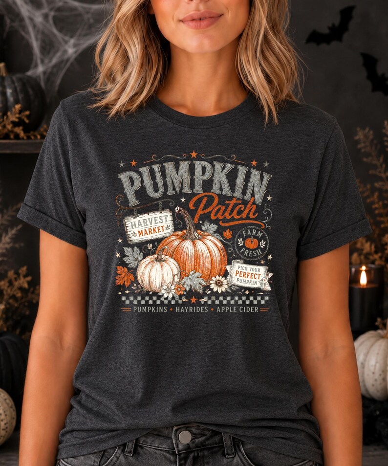 May include: A dark charcoal gray t-shirt featuring a graphic print with the text PUMPKIN PATCH, HARVEST MARKET, FARM FRESH, and PICK YOUR PERFECT PUMPKIN. The design includes two pumpkins, autumn leaves, flowers, and the words PUMPKINS, HAYRIDES, APPLE CIDER.