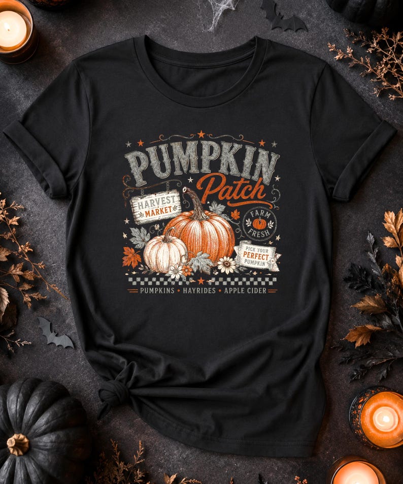 May include: A black t-shirt featuring a graphic print with the text PUMPKIN PATCH, HARVEST MARKET, FARM FRESH, and PICK YOUR PERFECT PUMPKIN. The design includes illustrations of two pumpkins, autumn leaves, flowers, and a checkered border pattern.