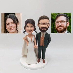 Puede incluir: Un adorno personalizado para pastel de boda con una novia y un novio en estilo de caricatura. La novia lleva un vestido de novia blanco y el novio lleva un traje verde oscuro con un chaleco marrón y una corbata azul claro. Ambas figuras tienen una cabeza grande y un cuerpo pequeño.