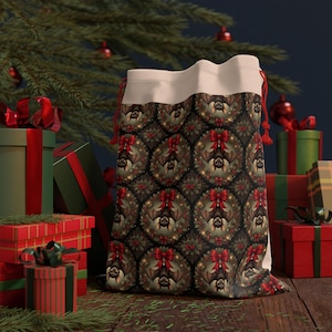 May include: A Christmas-themed gift bag with a repeating pattern of bats, wreaths, and red bows. The bag has a cream-colored top and red drawstring. Presents and a Christmas tree are in the background.