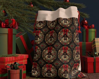 May include: A festive gift bag featuring a repeating pattern of bats, wreaths, and red bows. The bag has a cream-coloured top and red drawstring. Presents and a Christmas tree are in the background.