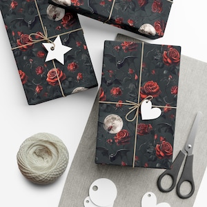 May include: Gift-wrapped presents with a dark floral pattern featuring red roses, bats, and moons. Each package is tied with twine and a white tag. A ball of twine, scissors, and blank tags are also visible.