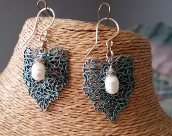 May include: A pair of silver filigree heart-shaped earrings with a white pearl dangling from each. The earrings have a teal green patina finish.