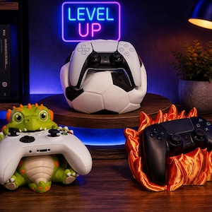 May include: Three video game controller stands: a white and black football holding a white controller, a green dragon figure holding a white controller, and a flame-shaped base holding a black controller, with a neon LEVEL UP sign.