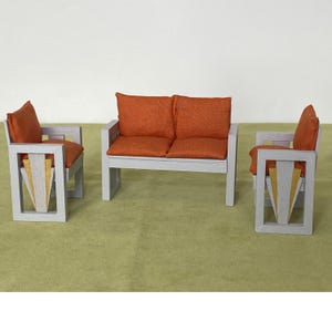 Può includere: Un set di mobili in legno grigio in miniatura con cuscini arancioni. Il set comprende un divano a due posti e due poltrone. Le poltrone hanno un design decorativo dorato e bianco sul davanti.