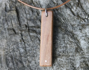 May include: A brown wooden pendant with a small white dot on the front, hanging from a brown leather cord.
