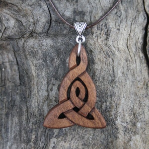 Puede incluir: Un collar con un colgante de madera con nudo celta y una anilla de plata. El colgante está tallado de forma intrincada y tiene un acabado de madera marrón.