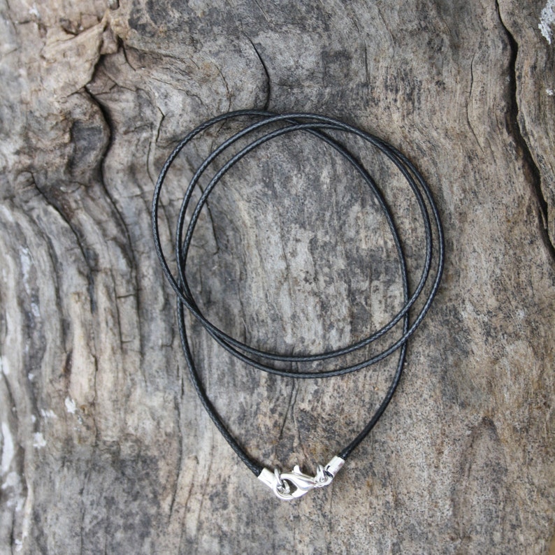 May include: A black leather cord necklace with a silver clasp. The cord is doubled over and the clasp is at the bottom of the image.