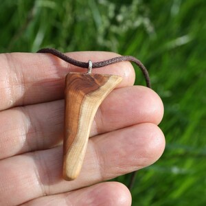 May include: A pendant featuring a smooth, triangular piece of polished wood with visible grain patterns in shades of light and dark brown. The wooden charm is suspended from a dark brown cord and attached with a small silver-colored metal bail.