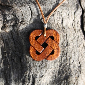 May include: A wooden pendant necklace with a brown Celtic knot design. The pendant is hanging on a brown leather cord.
