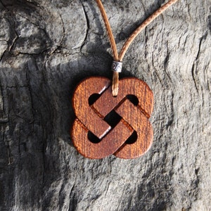 May include: A wooden pendant with a Celtic knot design, hanging from a brown cord. The pendant is brown and has a detailed knot pattern.
