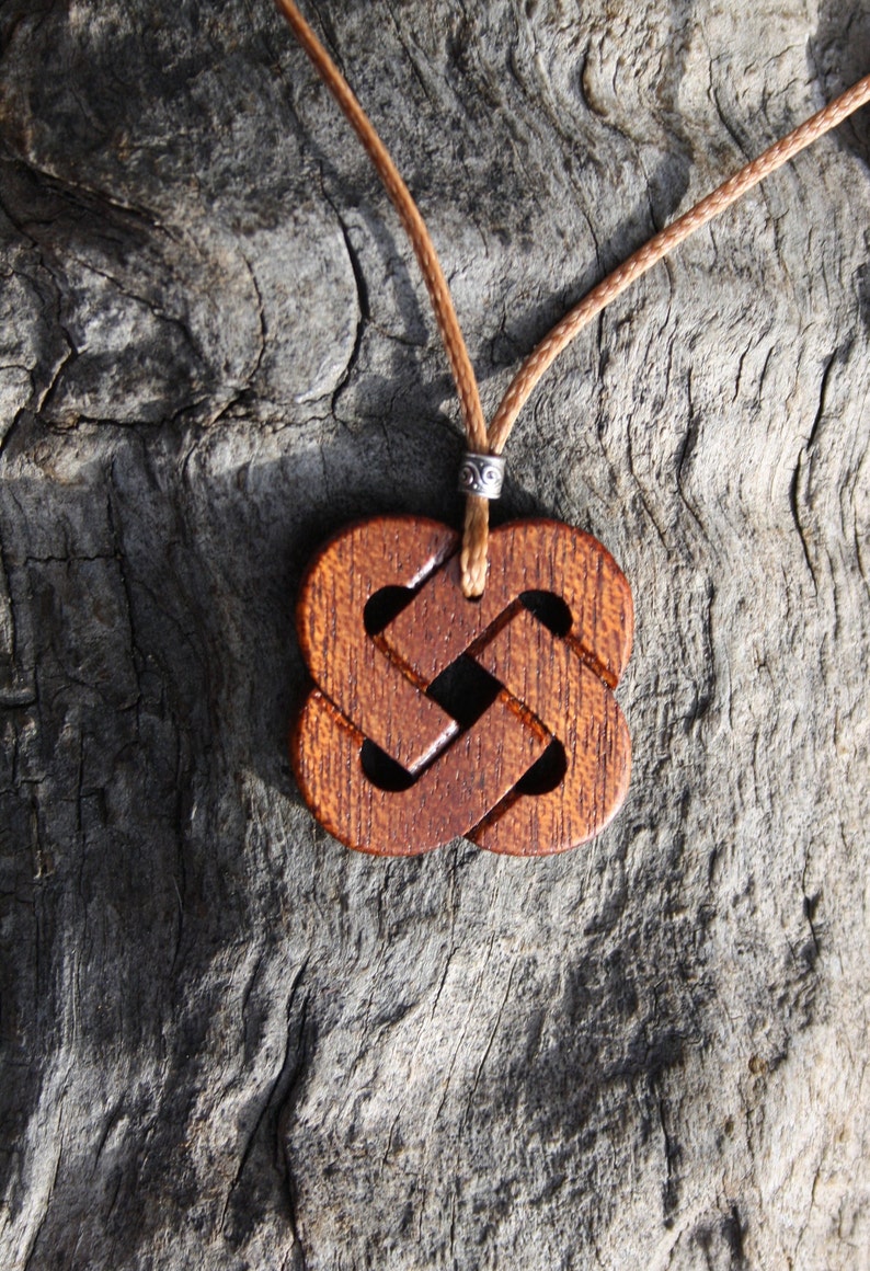 May include: A wooden pendant with a Celtic knot design, hanging from a brown cord. The pendant is brown and has a detailed knot pattern.