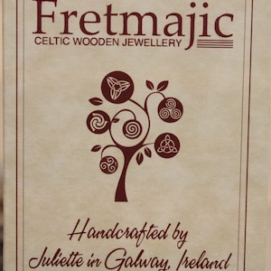 Pu&ograve; includere: Un cartoncino marrone con il testo "Fretmajic Celtic Wooden Jewellery" e un albero stilizzato con nodi celtici. Il testo "Handcrafted by Juliette in Galway, Ireland" &egrave; anche sul cartoncino.