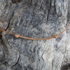May include: A close-up of a brown leather cord tied in a knot. The cord is lying on a piece of weathered wood.