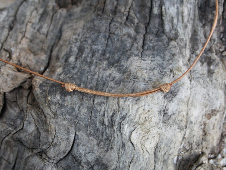 May include: A close-up of a brown leather cord tied in a knot. The cord is lying on a piece of weathered wood.