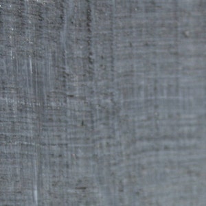 May include: Close-up of a textured, gray surface with visible grain and subtle variations in tone. The surface appears to be made of a rough material, possibly wood or a similar composite, with a slightly weathered appearance.