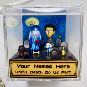 Könnte beinhalten: Ein pixeliges Diorama in einer transparenten Acrylbox, das eine Braut und einen Bräutigam mit einem Hund in einer Friedhofsszene zeigt. Der Hintergrund zeigt einen mondbeschienenen Himmel. Die Basis trägt den Text "Your Names Here Until Death Do Us Part".