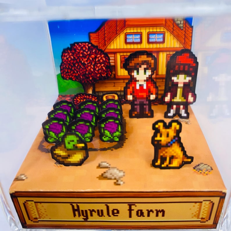 May include: A pixelated diorama featuring a farm scene with a house, trees, and crops. Two figures and a dog are present. The base of the diorama reads "Hyrule Farm" in gold lettering. The scene is enclosed in a clear box.