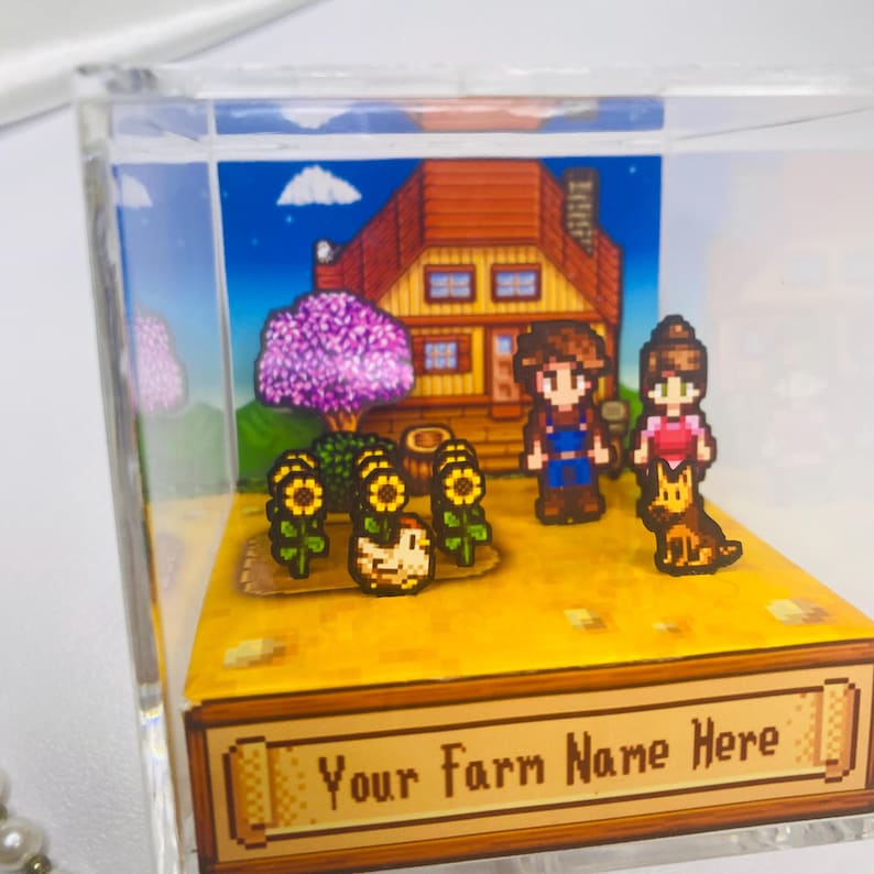 May include: A miniature diorama featuring a pixelated farm scene. It includes a house, characters, sunflowers, and a dog. The base has the text "Your Farm Name Here". The scene is enclosed in a clear acrylic box.
