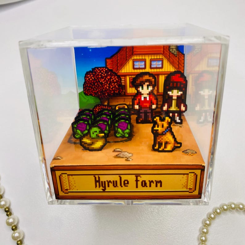 May include: A pixelated diorama inside a clear acrylic cube. The scene depicts a farm with a house, crops, two figures, and a dog. The base of the cube has the text "Hyrule Farm" in a gold frame.
