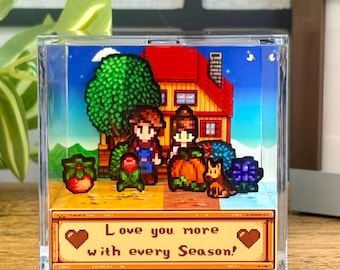 Puede incluir: Diorama pixelado que presenta una pareja, un perro y una casa con tejado rojo. La escena incluye un árbol, flores y una calabaza. El texto "Love you more with every Season!" se muestra en la parte inferior.