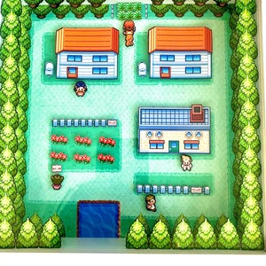 May include: A framed, pixelated artwork depicting a town scene with houses, trees, and characters. The houses have orange roofs and blue windows. The artwork is set against a green background, with a blue pond and a white frame.