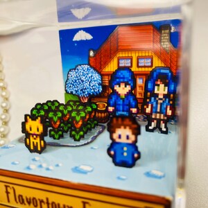 May include: A pixelated diorama featuring characters and elements from a video game. The scene includes a house, trees, crops, and several figures in blue attire. The background is a blue sky with clouds. The base of the diorama has the word "Flavortown".