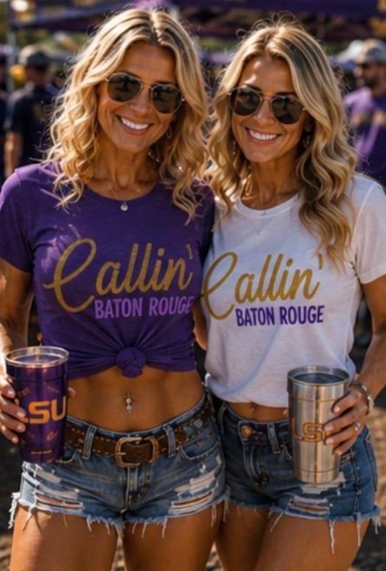 Puede incluir: Dos camisetas con el texto Callin' Baton Rouge en dorado y morado. Una camiseta es morada con texto dorado y la otra es blanca con texto dorado y morado. Ambas se combinan con pantalones cortos de mezclilla desgastados y vasos de metal.