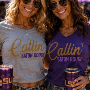 Puede incluir: Una camiseta gris y una camiseta morada, ambas con el texto dorado Callin' Baton Rouge en letras moradas y doradas. Cada prenda se combina con pantalones cortos de mezclilla azul y un vaso morado con el logotipo amarillo LSU impreso.