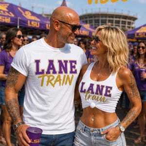 May include: A white crew-neck t-shirt and a white sleeveless tank top, both featuring the purple and gold text LANE TRAIN. The t-shirt has block lettering, while the tank top has a knotted hem and a mix of block and script lettering.