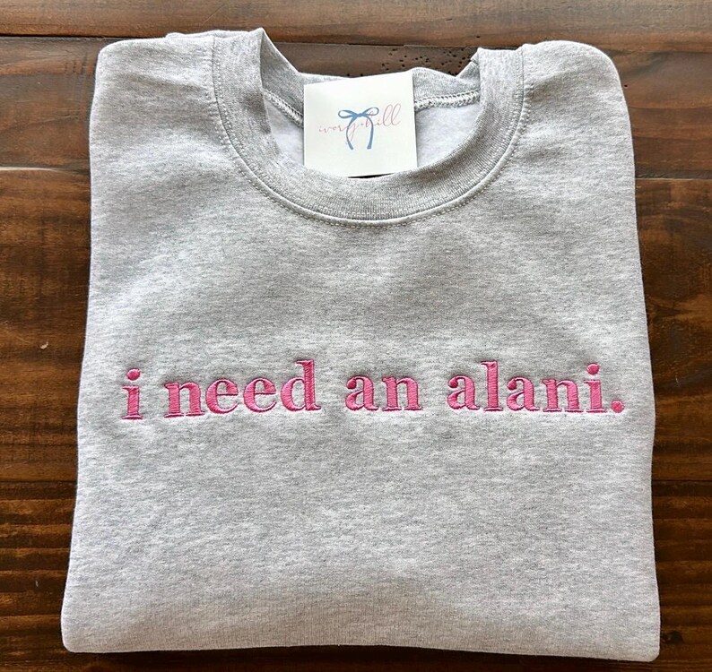 May include: Gray sweatshirt with the text "i need an alani." embroidered in pink.