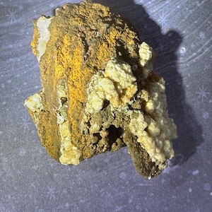 May include: A natural mineral specimen with a rough, textured surface. The rock displays a mix of colours, including yellow, brown, and white. The mineral has a crystalline structure and appears to be a geode or similar rock formation.