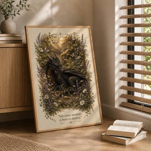 Könnte beinhalten: Ein gerahmter vertikaler Kunstdruck, der einen dunklen Drachen zeigt, der in einer üppigen Waldlichtung zwischen Lavendel und weißen Gänseblümchen ruht. Der Text "Not every monster is born to destroy." ist unten auf dem cremefarbenen Druck zu sehen.