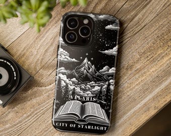 May include: A black smartphone case featuring a white graphic illustration of a mountain range under a starry night sky with clouds, pine trees, and an open book at the bottom. The text VELARIS CITY OF STARLIGHT is printed on the phone case.
