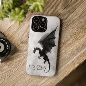 May include: A white smartphone case featuring a black silhouette of a dragon in flight against a cloudy background. The text "IT'S BEEN my honor" is printed in black near the bottom. The case has a cutout for a triple-lens camera system.