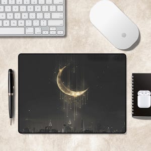 Puede incluir: Una alfombrilla de rat&oacute;n rectangular con un fondo de cielo nocturno oscuro y una gran luna creciente dorada y brillante. Finas l&iacute;neas verticales doradas cuelgan de la luna sobre la silueta de un horizonte urbano en la parte inferior.