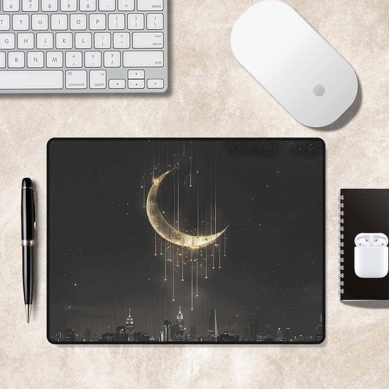 Puede incluir: Una alfombrilla de rat&oacute;n rectangular con un fondo de cielo nocturno oscuro y una gran luna creciente dorada y brillante. Finas l&iacute;neas verticales doradas cuelgan de la luna sobre la silueta de un horizonte urbano en la parte inferior.