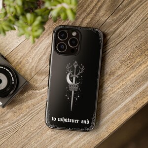 May include: Black phone case featuring a silver emblem of a sword, crown, and crescent moon with deer antlers. The text "to whatever end" is at the bottom. The case has a decorative border.