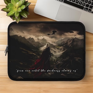 Op de afbeelding: Zwarte laptoptas met een fantasielandschap. Het toont een figuur in een rode cape, een draak en bergen. De tekst "from now until the darkness claims us" is inbegrepen.