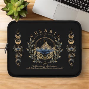 以下が含まれることがあります： 「VELARIS - CITY OF STARLIGHT」の文字と山と花の模様が特徴の黒いノートパソコンスリーブ。スリーブには「To the stars who listen and the dreams that are answered」という引用句も含まれています。
