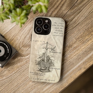 May include: A phone case with a detailed illustration featuring a sword, mountains, and roses. The design includes the phrases "Light it up", "To whatever end", and "I will not be afraid". The case has a neutral color palette.
