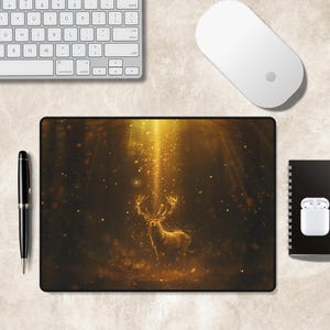 Puede incluir: Una alfombrilla de rat&oacute;n rectangular con una ilustraci&oacute;n digital de un ciervo dorado brillante de pie en un bosque oscuro. El ciervo est&aacute; iluminado por un haz de luz vertical brillante y rodeado de part&iacute;culas doradas sobre fondo oscuro.