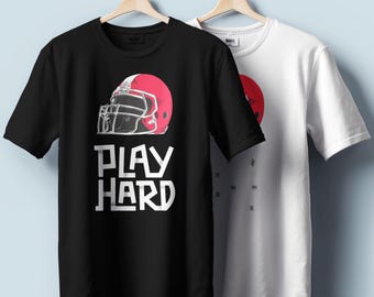 Könnte beinhalten: Zwei T-Shirts hängen an Holzbügeln. Eines ist schwarz mit einer weißen Grafik eines Footballhelms und den Worten "PLAY HARD" in Weiß. Das andere ist weiß mit einer roten Kreisgrafik. Beide Shirts haben kurze Ärmel.